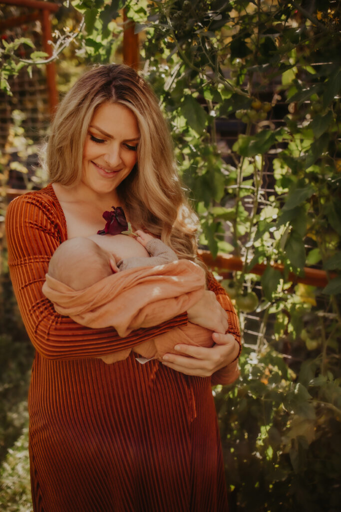 A tender moment of a mother nursing newborn baby in a lush garden setting, the mother cradling the infant closely. The image captures the intimacy of early parenthood, highlighting the importance of nurturing moments. Newborn photo shoot Edmonton.