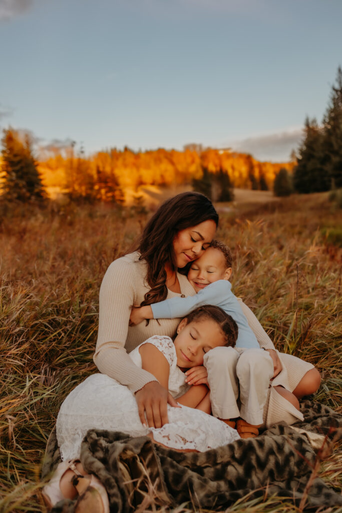 a mom snuggles her son and daughter while snuggling on the grass during a family photo shoot in Edmonton