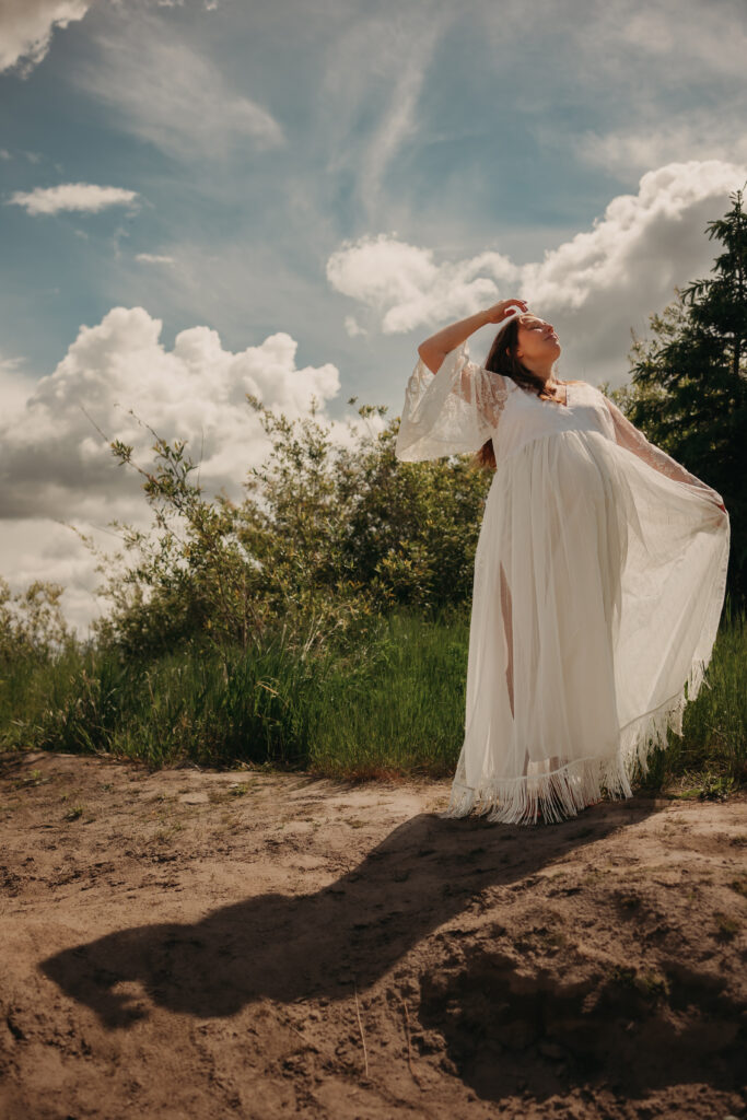 Pregnant woman in ethereal white lace dress poses for dreamy maternity photos during her maternity photo shoot in Edmonton