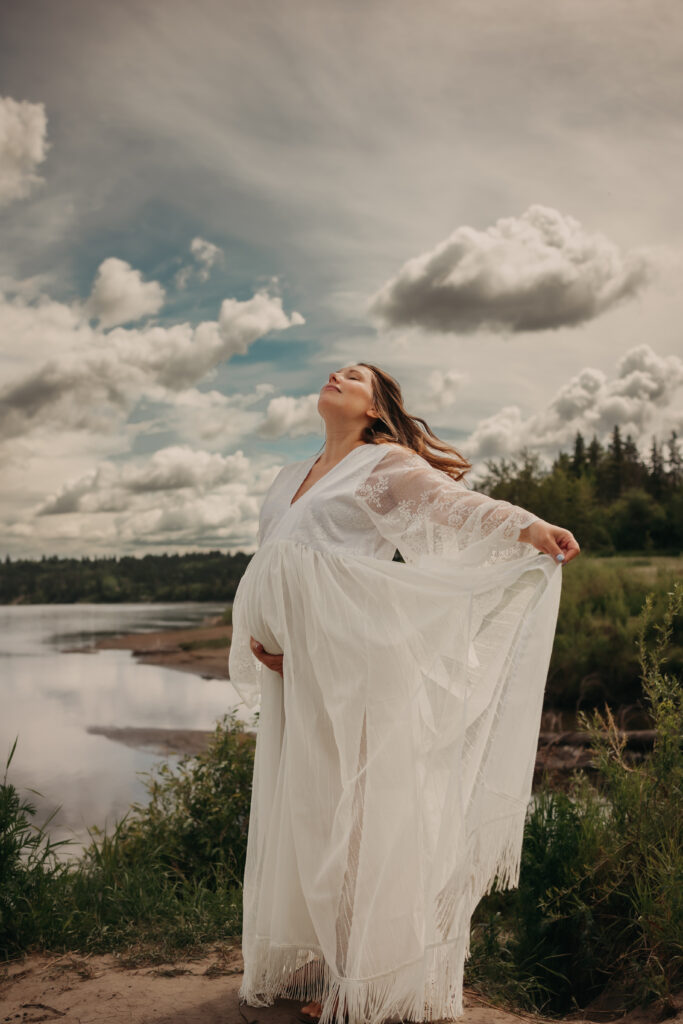 Pregnant woman in ethereal white lace dress poses for dreamy maternity photos in Edmonton