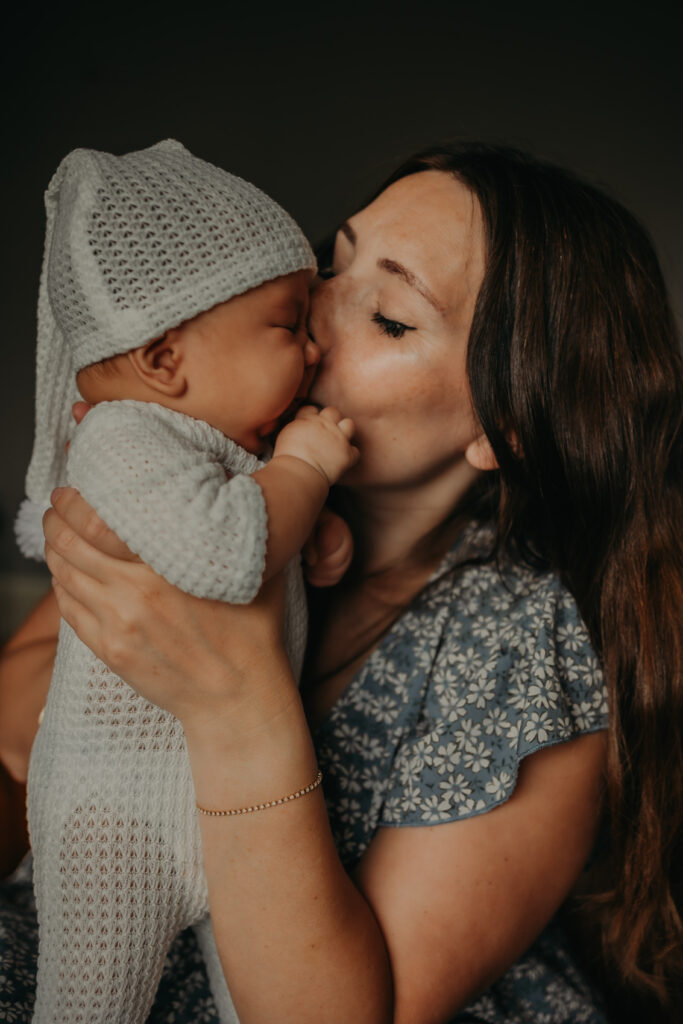 A mom in a light blue dress kisses her newborn baby on the cheek during her newborn photoshoot in Edmonton