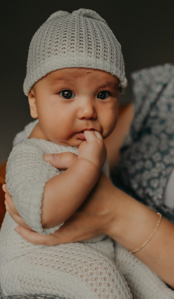 newborn baby wearing a white knit cap and romper during a newborn photo session in Edmonton held in his mother's hands