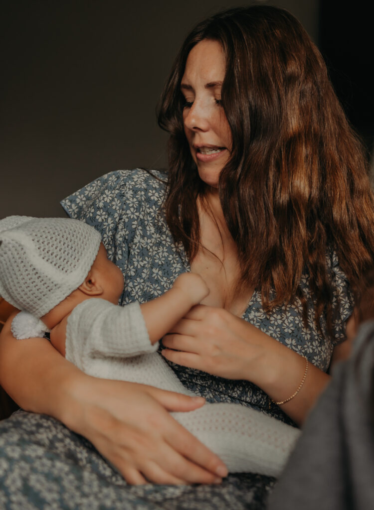 A mom in a light blue dress looks down at her newborn baby during her newborn photoshoot in Edmonton