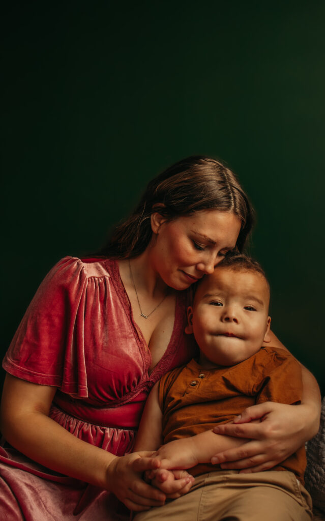 A mom in a pink dress cuddles her son during an indoor family photo session in Edmonton, Alberta