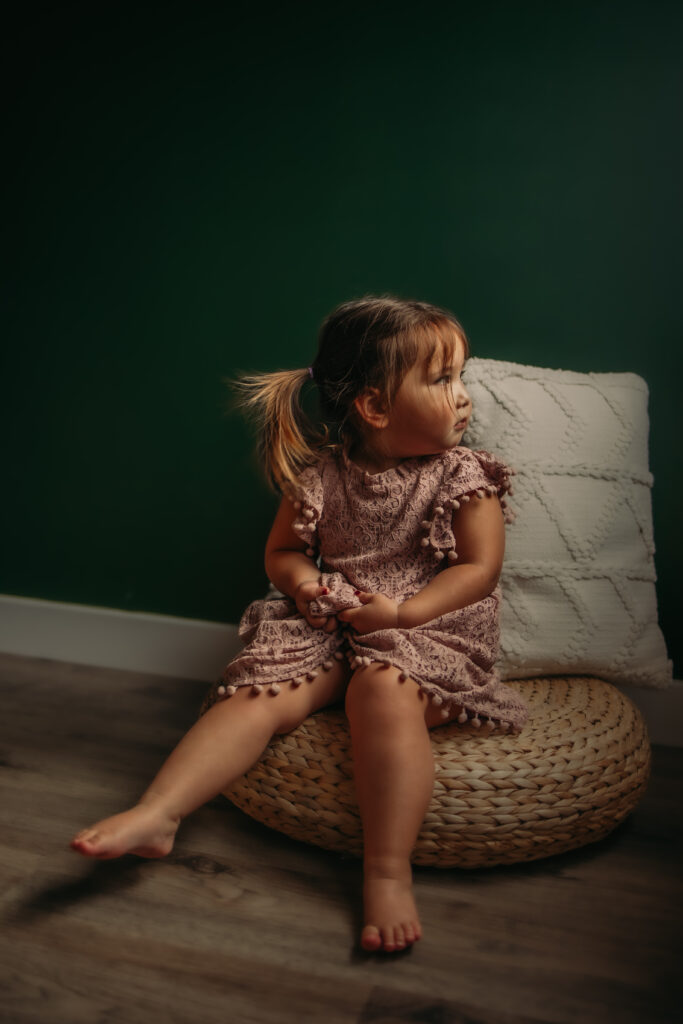 a toddler girl looks out the window during her indoor family photo session in Edmonton, Alberta