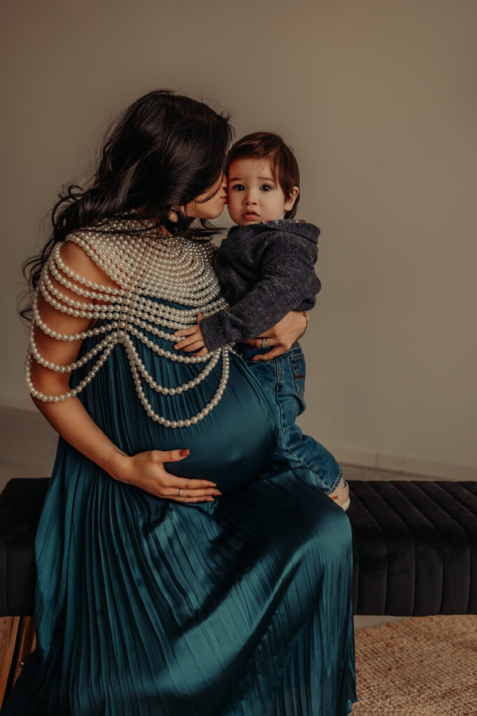 Mom in a blue dress holds toddler son during an indoor Edmonton maternity photo shoot