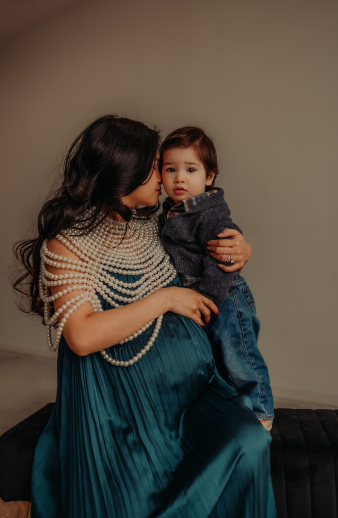 Mom in a blue dress holds toddler son during Edmonton maternity photo shoot