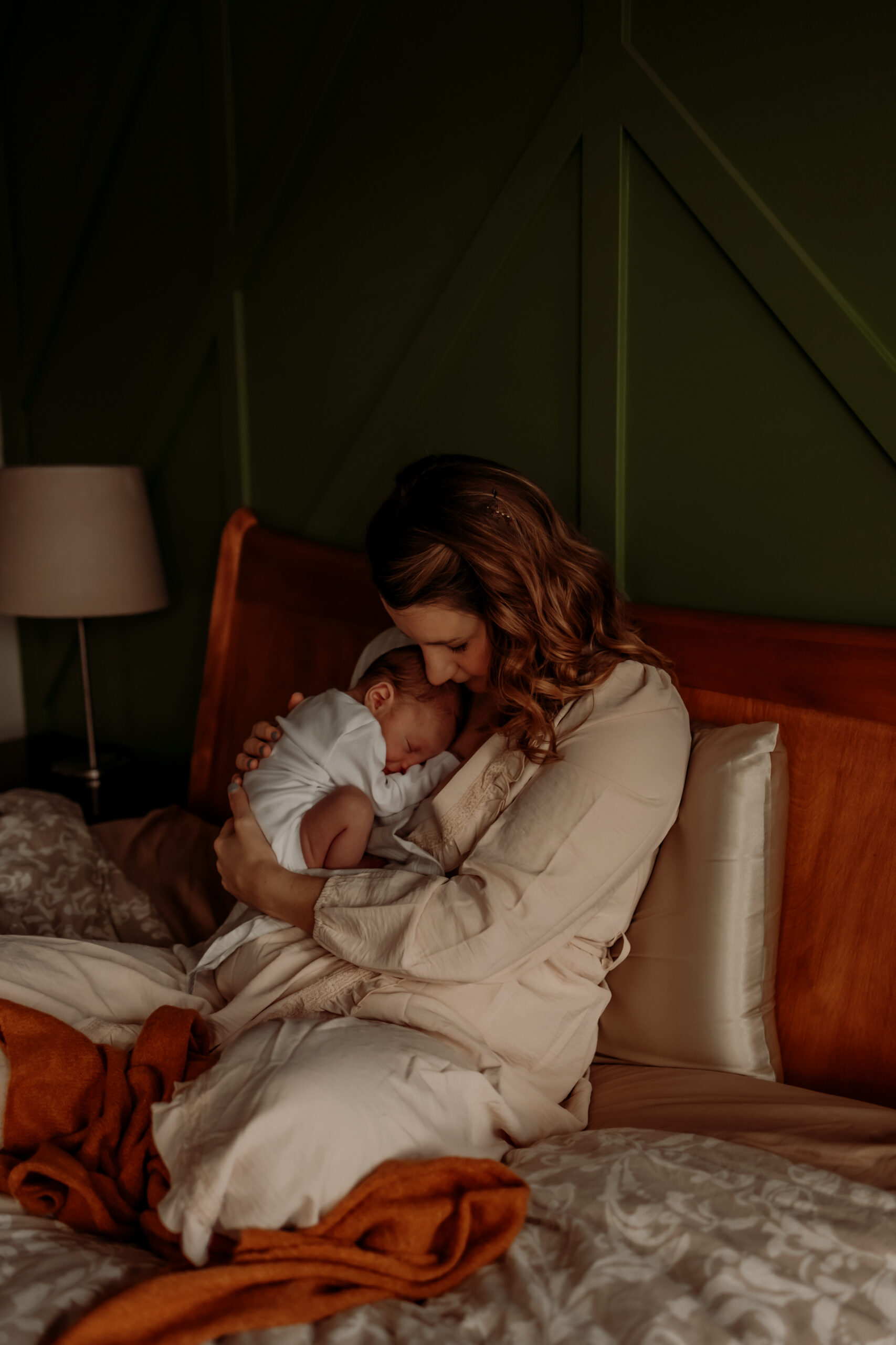 a mother snuggles her newborn son on a bed during an edmonton cozt newborn shoot at home