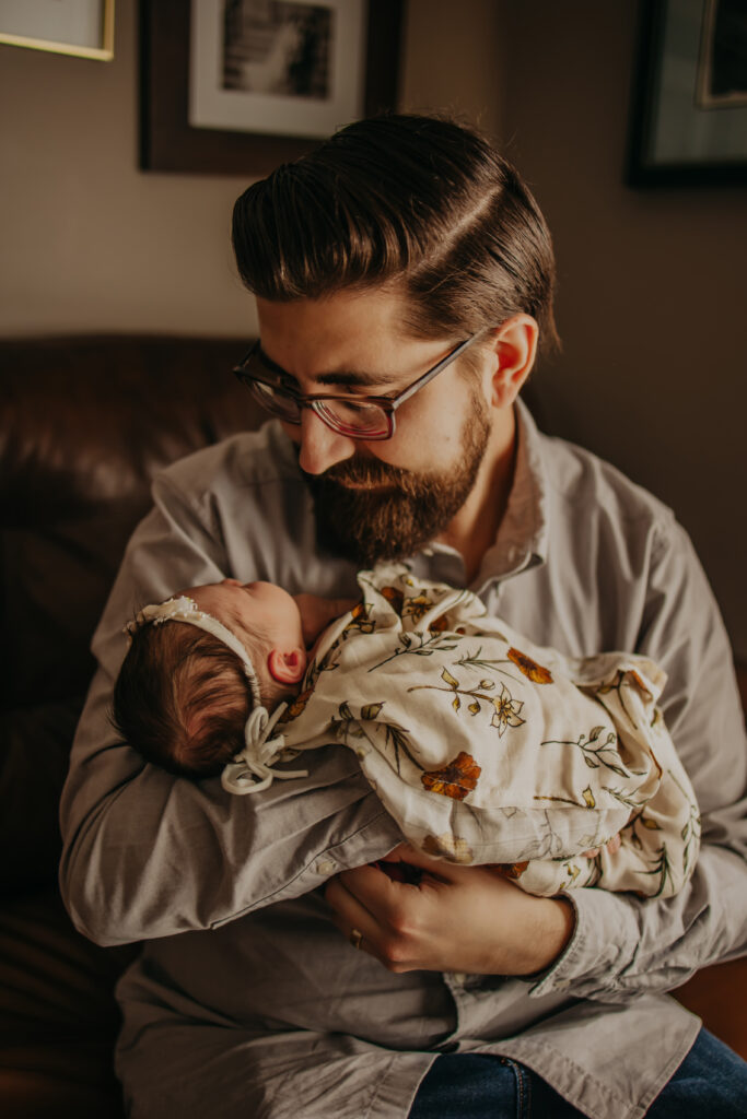 dad holds baby daughter and looks at her during Edmonton newborn photo session